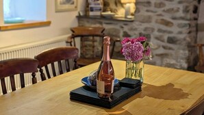 A wooden table with a bottle of rose wine, a vase of pink flowers, and a stack of black coasters.