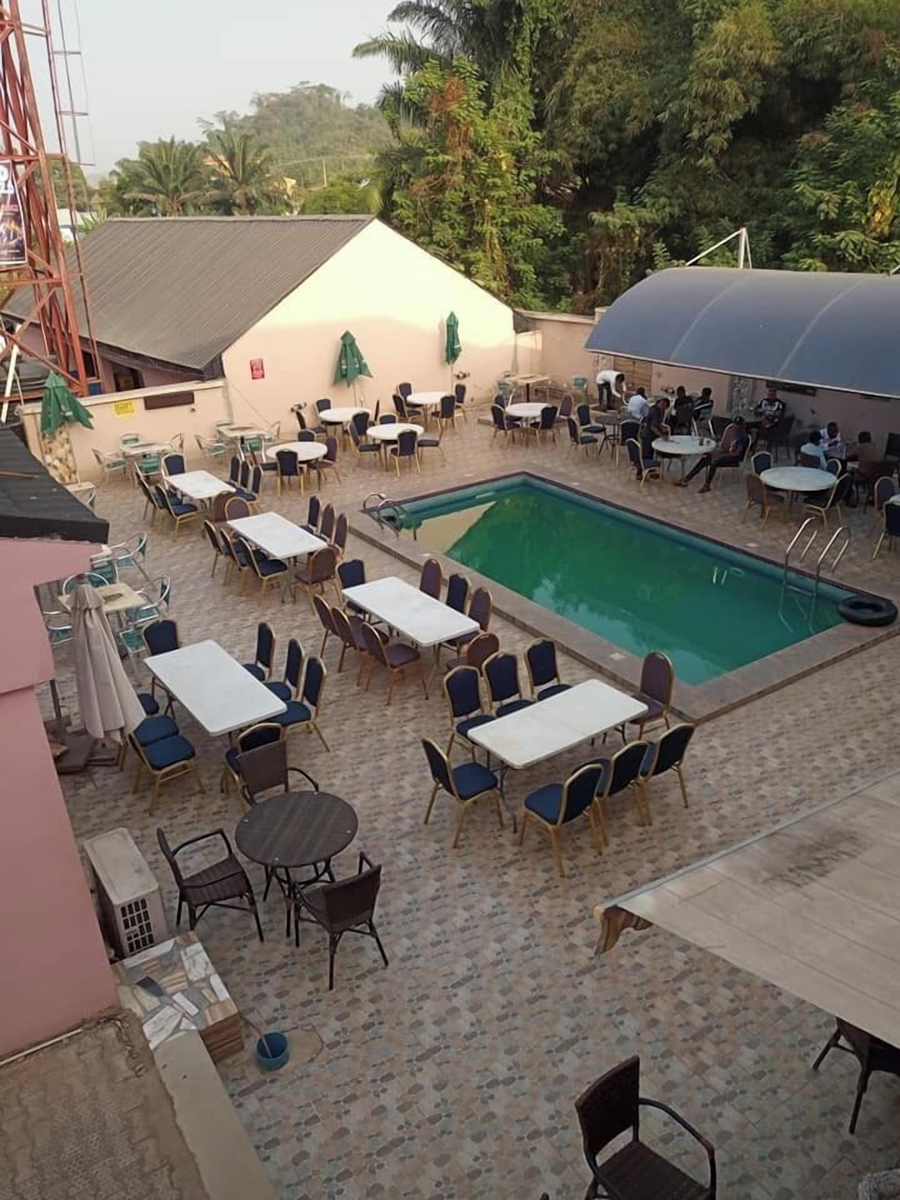 Ett utomhusområde med en pool, flera bord och stolar, omgivet av en plattlagd uteplats.