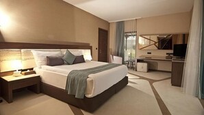 Een moderne hotelkamer met een groot bed, nachtkastje en een werkplek met stoel en televisie.