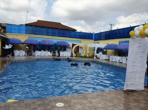 An indoor swimming pool with a tiled floor, surrounded by white tables and blue umbrellas. - Hotel Valerie Suites (Asaba)