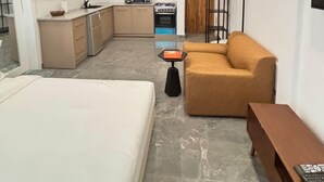 Une chambre d’hôtel compacte comprenant un lit, un canapé, une petite table, un téléviseur et une kitchenette.