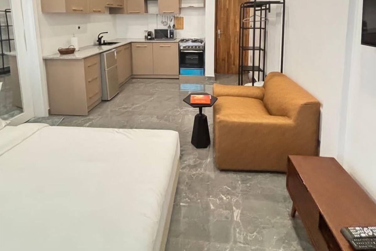 A compact hotel room with a bed, a sofa, a small table, a TV, and a kitchenette.