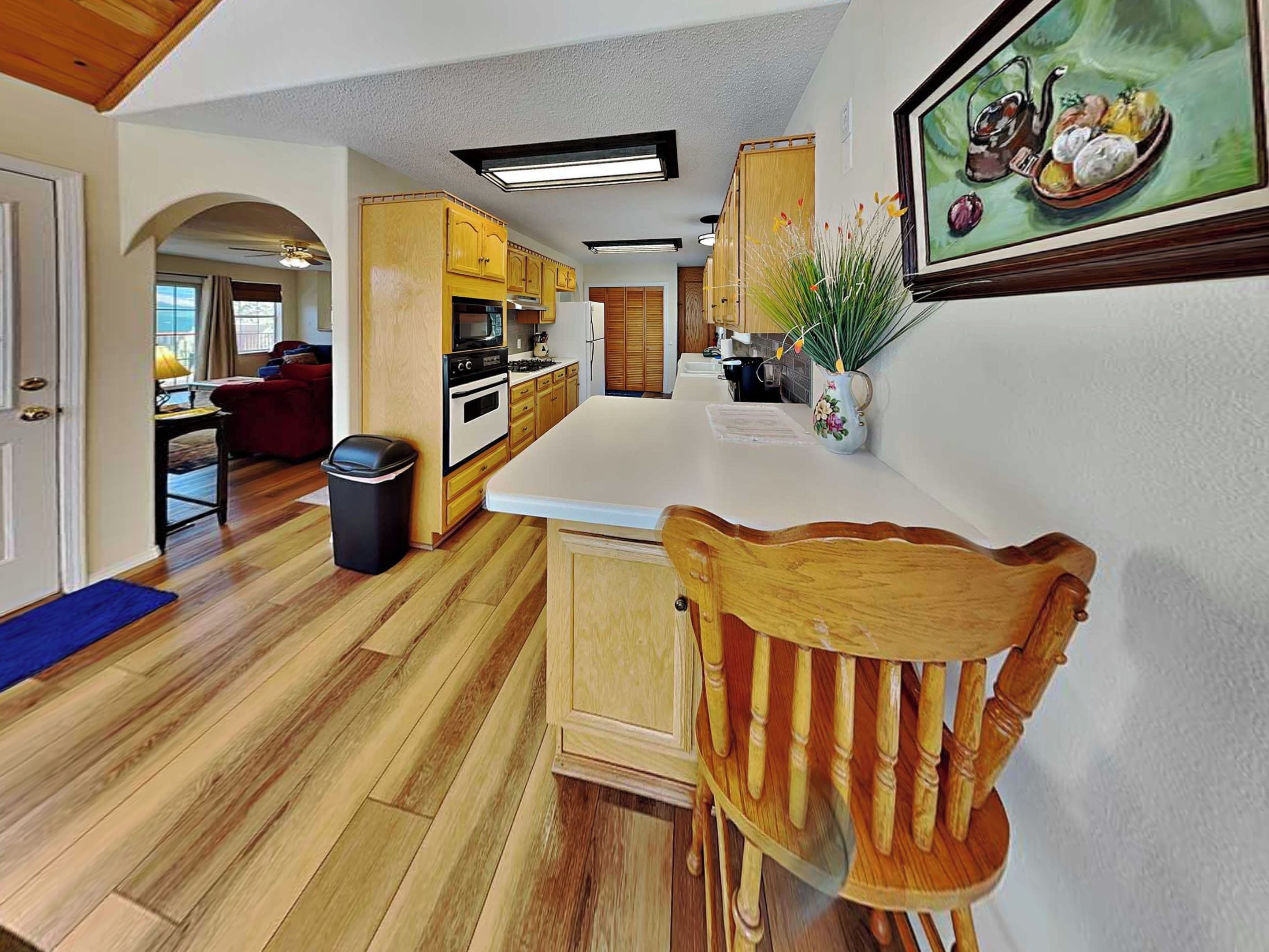 A kitchen with wooden cabinets, a white countertop, and a dining area with a wooden chair.