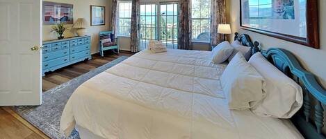 A bedroom with a large bed, a ceiling fan, a dresser, and a window with curtains.