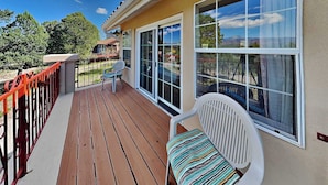 A wooden deck with a white chair and a red railing, large windows with a view of trees and a mountain.