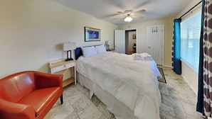 A hotel room with a bed, a desk, a chair, a ceiling fan, and a window with curtains.
