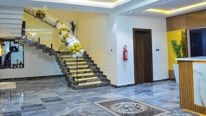 A modern hotel lobby with a marble staircase, a reception desk, and a fire extinguisher. - RKD SUITES Asaba (Asaba)
