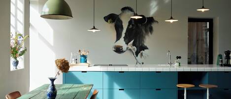 A modern kitchen with blue cabinets, a hanging light fixture, and a large wall-mounted cow decoration.