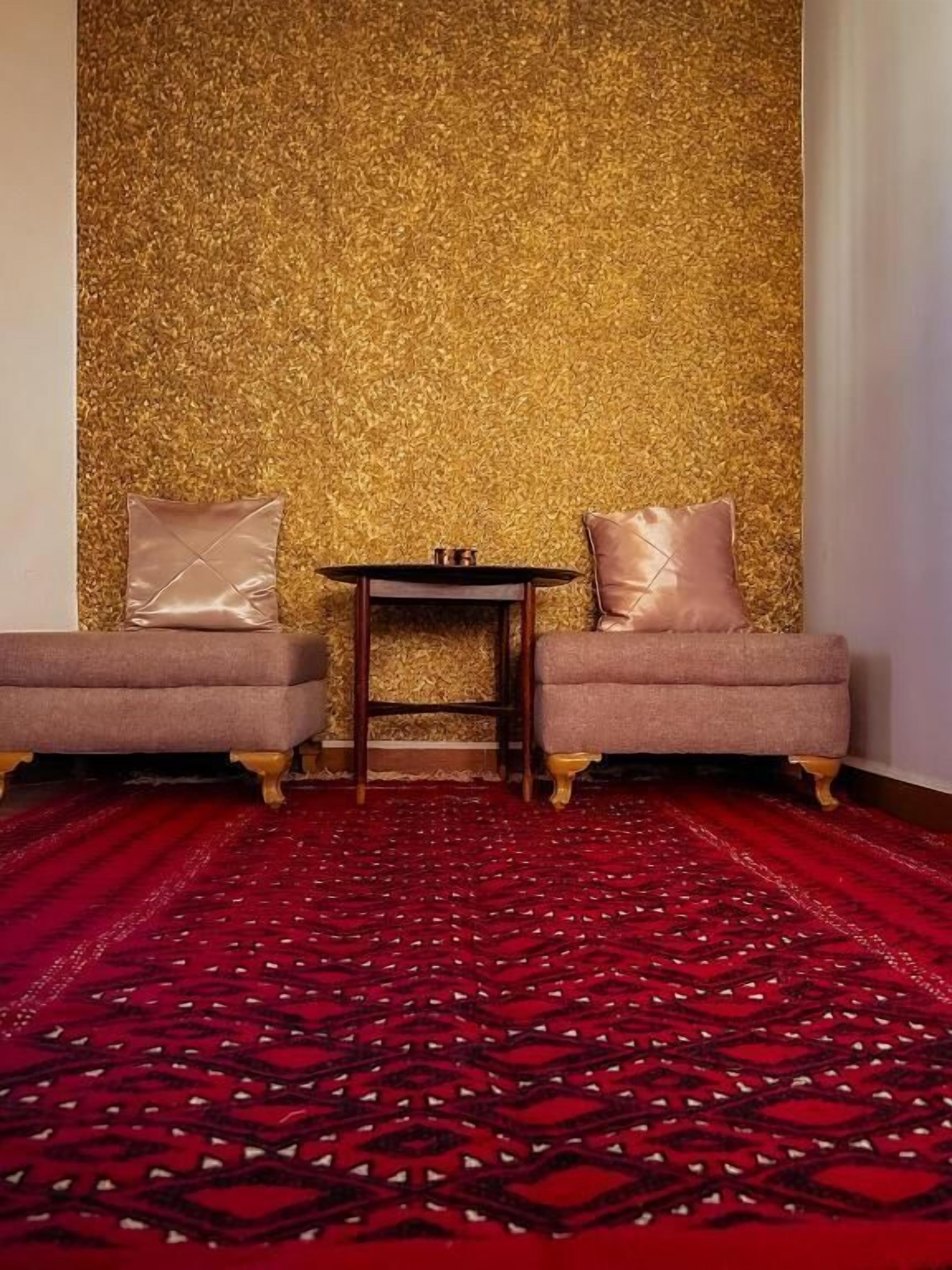 Una habitación con dos sillones, una mesita y una alfombra roja estampada.