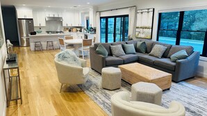 A modern living room with a sectional sofa, ottomans, and a dining area with a kitchen in the background.