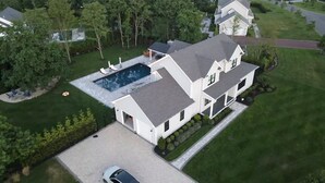 A two-story house with a swimming pool, a covered patio, and a well-maintained lawn.