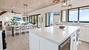 A spacious kitchen with a large island, white cabinetry, and a view of the ocean. - Stay Blessed Villa - Always Sandy Beach - Walkable To Restaurant By Beach! (Farmer's Hill)