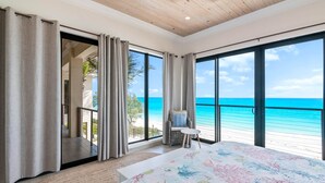 A bedroom with a large bed, a view of the beach, and a balcony with a chair. - Stay Blessed Villa - Always Sandy Beach - Walkable To Restaurant By Beach! (Farmer's Hill)