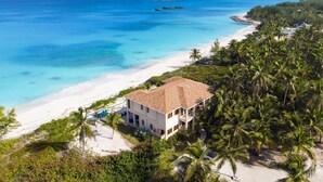 A beachfront property with a white building, a sandy beach, and a clear blue ocean. - Stay Blessed Villa - Always Sandy Beach - Walkable To Restaurant By Beach! (Farmer's Hill)