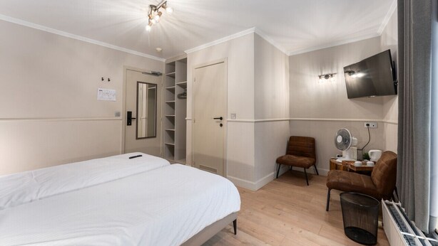 Un dormitorio con una cama, un armario, un televisor, una silla y una mesita de noche con un ventilador.