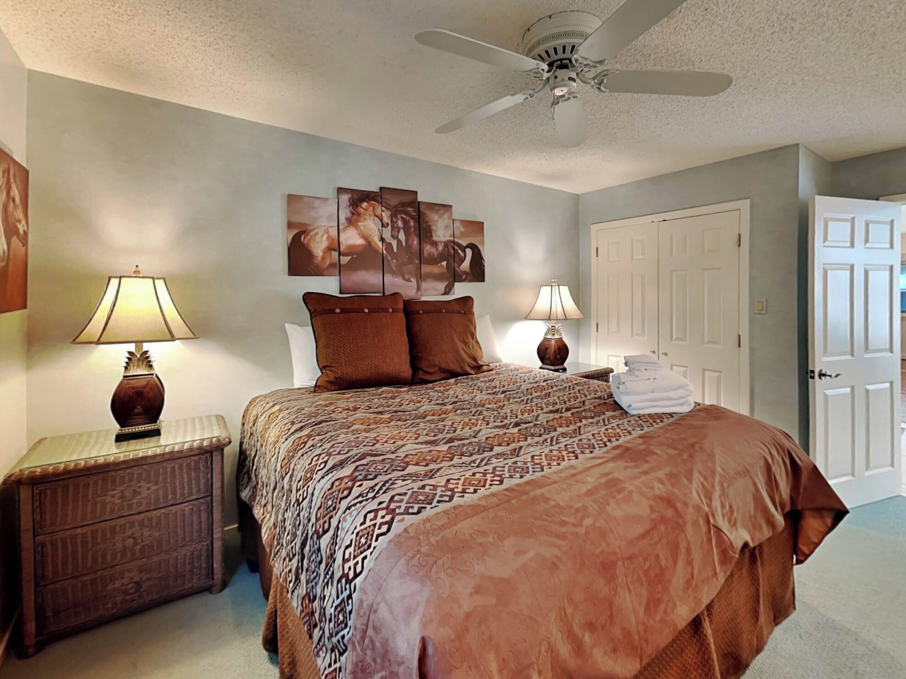 A bedroom with a bed, two nightstands, a ceiling fan, and a door.