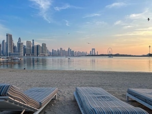 A beach with lounge chairs and a city skyline in the background.