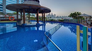 Una piscina con un pabellón circular, el horizonte de una ciudad al fondo y vista al agua.