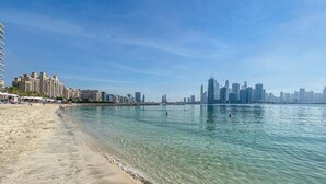 Una playa con agua cristalina, un horizonte urbano al fondo y una hilera de edificios a la izquierda.