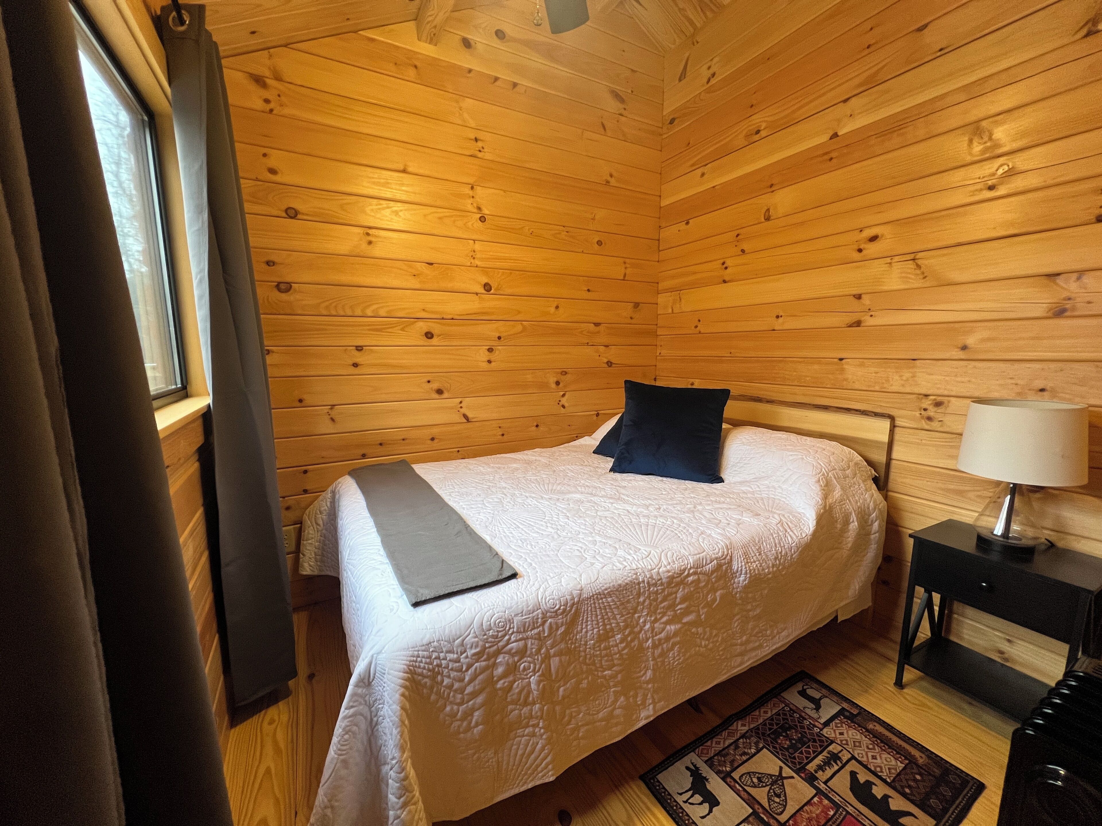 Habitació amb panells de fusta, un llit, una làmpada de nit i una catifes.
