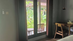 Une pièce comprenant un lit, une petite table en bois avec une chaise, une fenêtre donnant sur un espace verdoyant et un luminaire fixé au mur.