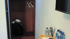Un couloir avec une armoire en bois, un portant à vêtements, un plateau avec des bouteilles et une télécommande, et une poubelle noire.