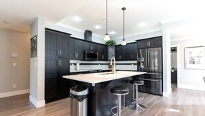 Una cucina moderna con mobili scuri, un'isola centrale con sgabelli, elettrodomestici in acciaio inossidabile e illuminazione a sospensione.
