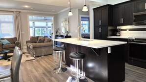 Una cucina moderna con mobili scuri, un'isola centrale con sgabelli e un'area pranzo con divano e sedie.