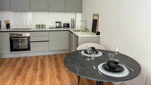 A modern kitchen with grey cabinets, a built-in oven, and a dining area with a round table set for two. - Modern Leeds Central Stay -2 min walk from station (Leeds)