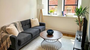 A living room with a dark grey sofa, a round coffee table, and a window with a view of a brick building. - Modern Leeds Central Stay -2 min walk from station (Leeds)