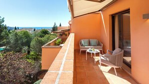 A balcony with a sofa, a small table, and a chair, overlooking a coastal area with trees and buildings. - Genteel Home Costa Nagüeles (Marbella)