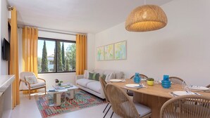 A modern living room with a dining area, featuring a large window, a sofa, a coffee table, and a dining table set for four. - Genteel Home Costa Nagüeles (Marbella)