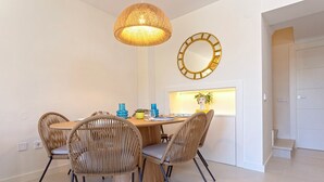 A dining area with a round table, four wicker chairs, a hanging light fixture, and a wall-mounted mirror. - Genteel Home Costa Nagüeles (Marbella)