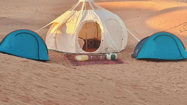 A tent set up in a desert with sand dunes in the background.