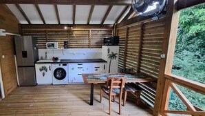 Een praktische keuken met een spoelbak, magnetron en een kleine koelkast. Er is een eettafel met stoelen en een houten terras buiten.