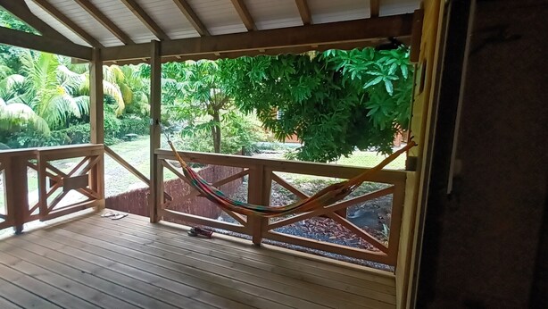 Een houten terras met een hangmat en een tafel, met uitzicht op een weelderige tuin met diverse planten en bomen.