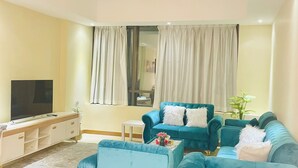 Ein Wohnzimmer mit blauem Sofagarnitur, einem Flachbildfernseher und einem kleinen Tisch mit einer Pflanze.