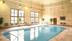 An indoor swimming pool with clear water, surrounded by chairs and potted plants.