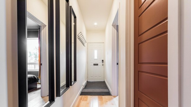 A hallway with a wooden floor, a brown door, and a white door at the end. - HOMA-Comfort&Style-2BR-Spacious-Natural Light-FeelHome-A/C-SelfCheckIn-Metro (Montréal)