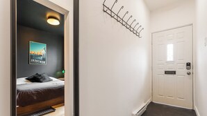 A hotel room with a bed, a wall-mounted coat rack, a door with a peephole, and a poster on the wall. - HOMA-Comfort&Style-2BR-Spacious-Natural Light-FeelHome-A/C-SelfCheckIn-Metro (Montréal)