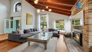 Ein geräumiges Wohnzimmer mit einem großen Ecksofa, einem Glastisch, einem Kamin und Blick ins Freie.