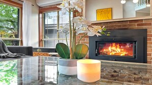 Ein Wohnzimmer mit Glastisch, Blumentopf, brennender Kerze und Kamin.