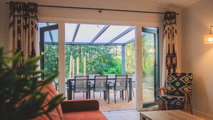 Ein modernes Wohnzimmer mit einer Couch, einem Tisch und einem Sessel. Eine Glastür führt zu einem Außenbereich mit Tisch und Stühlen.