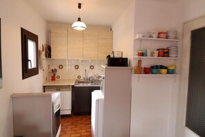 Cocina compacta con armarios de madera, lavavajillas integrado y una variedad de tazas coloridas en estantes.