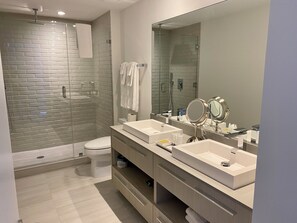 A modern bathroom with two sinks, a large mirror, and a glass-enclosed shower.