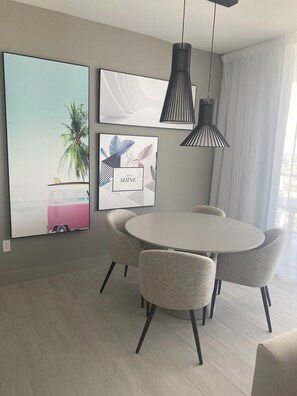 A modern dining area with a round table and four chairs, a ceiling light fixture, and two framed artworks on the wall.