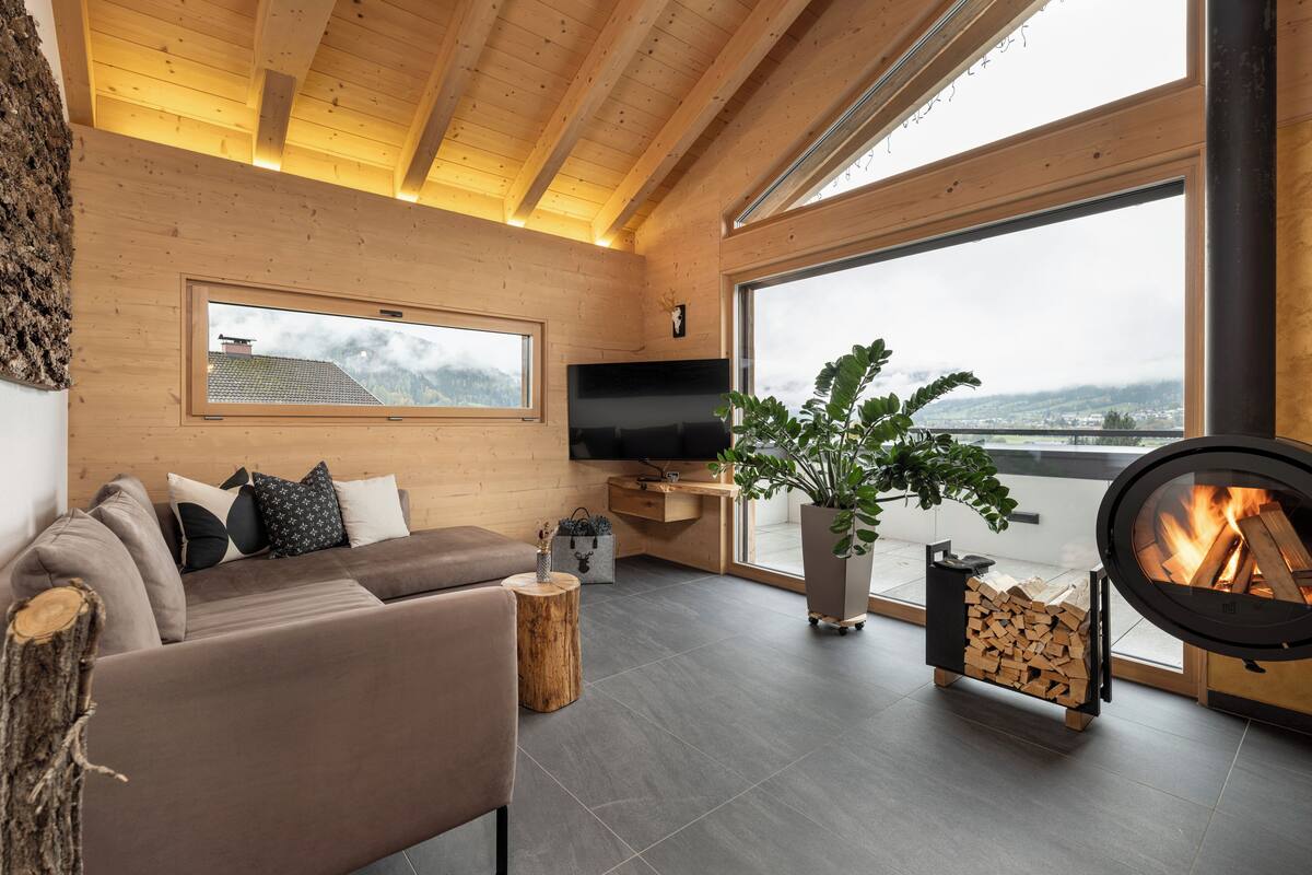A modern living room with a sofa, TV, fireplace, and large windows offering a view of the outdoors.