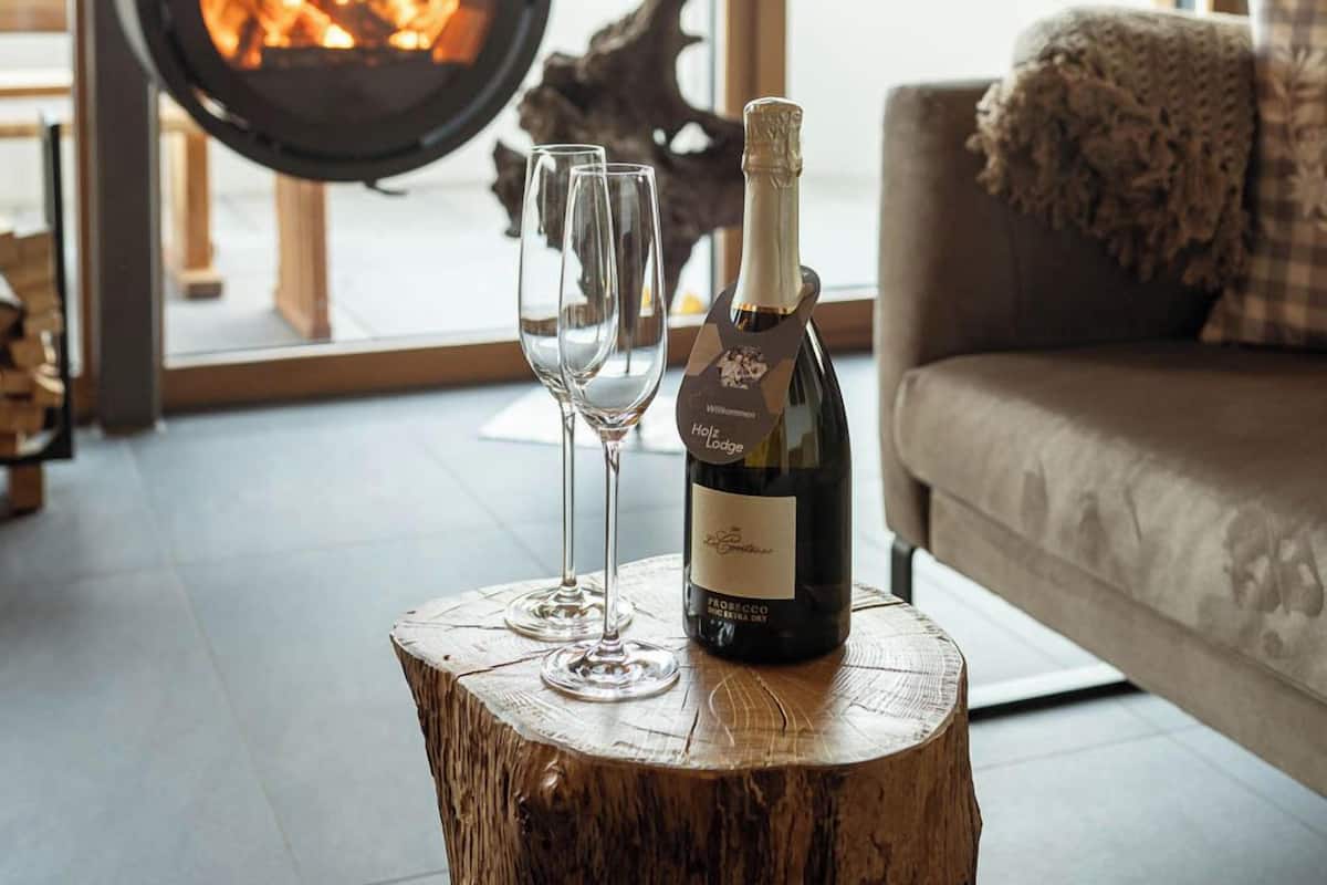 A cozy living room with a wood-burning stove, a bottle of wine, and two glasses on a tree stump.