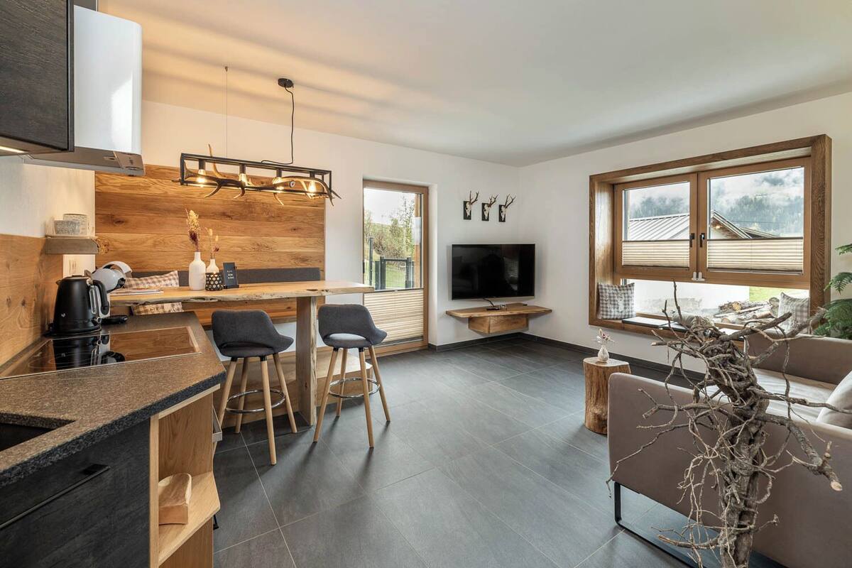 A modern kitchen with a wooden island, bar stools, a TV, and a seating area with a view of the outdoors.