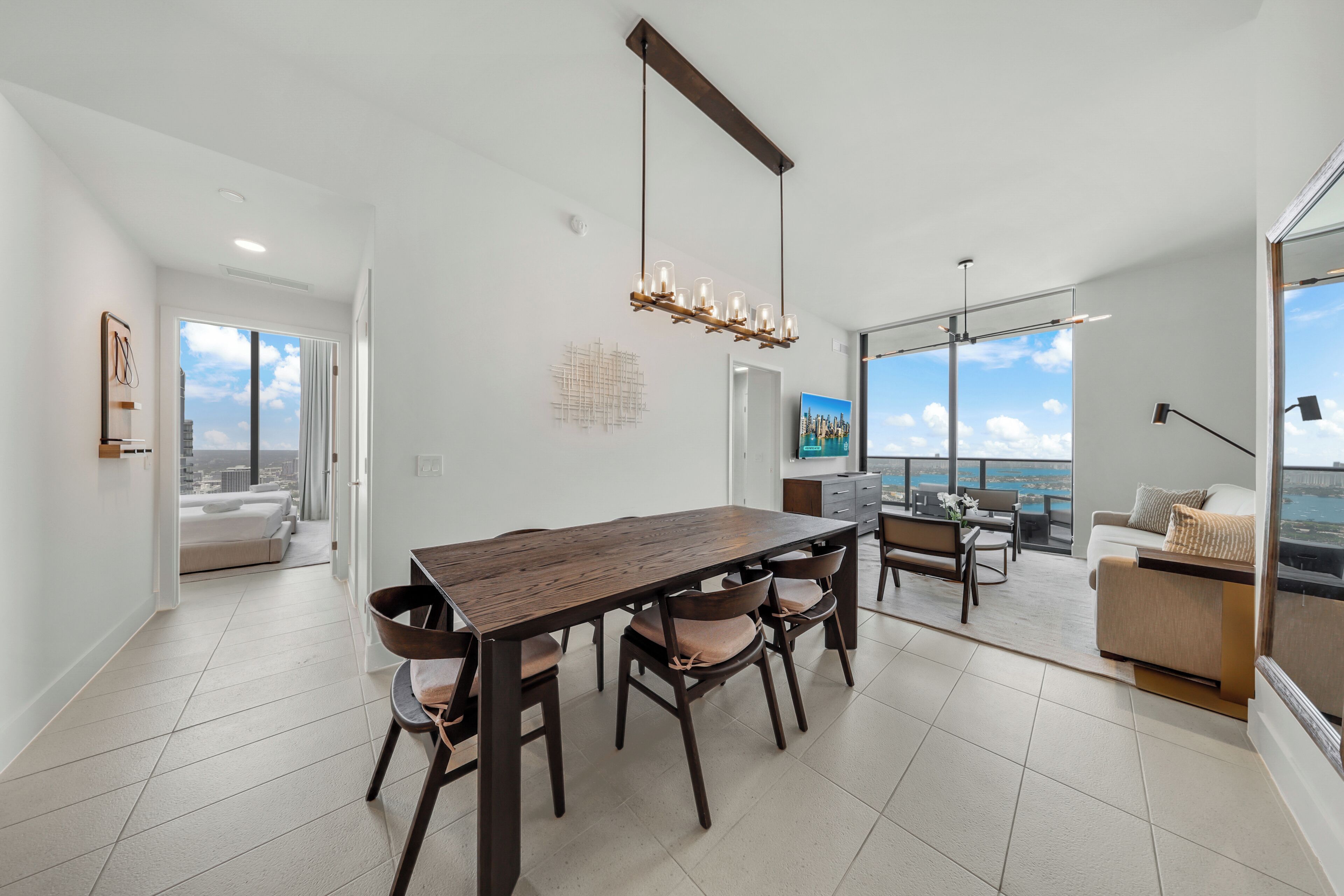 A modern dining area with a wooden table and chairs, a chandelier, and a view of the city.